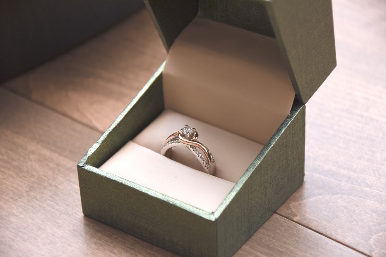 An mixed-metal solitaire diamond ring with a split shank design in an open green jewelry box.