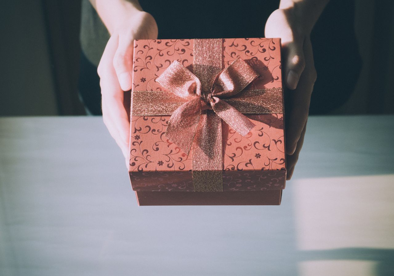 A person presenting a decorative gift box wrapped in patterned paper with a shiny ribbon and bow.