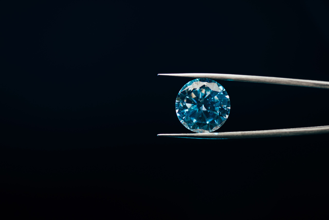 non-conflict diamond in blue hue held in tweezers