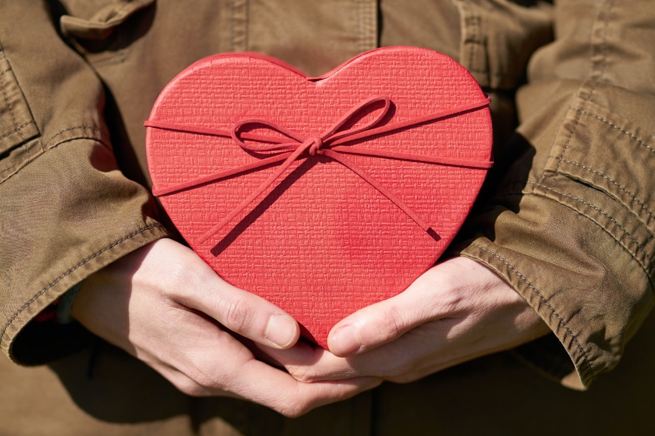 A man holding a red heart shaped box with a matching bow to give to his Valentine