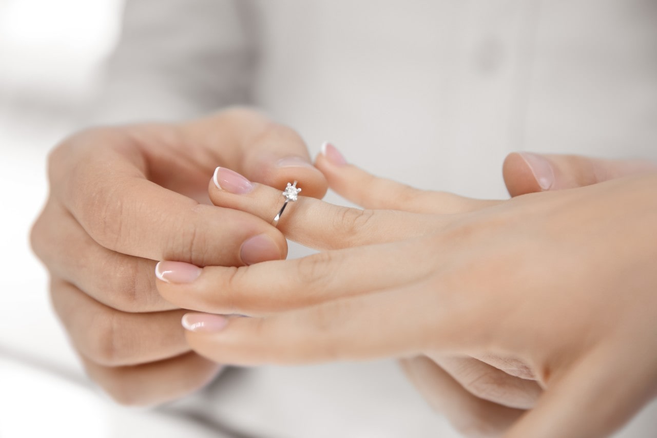 man placing solitaire engagement ring on hand